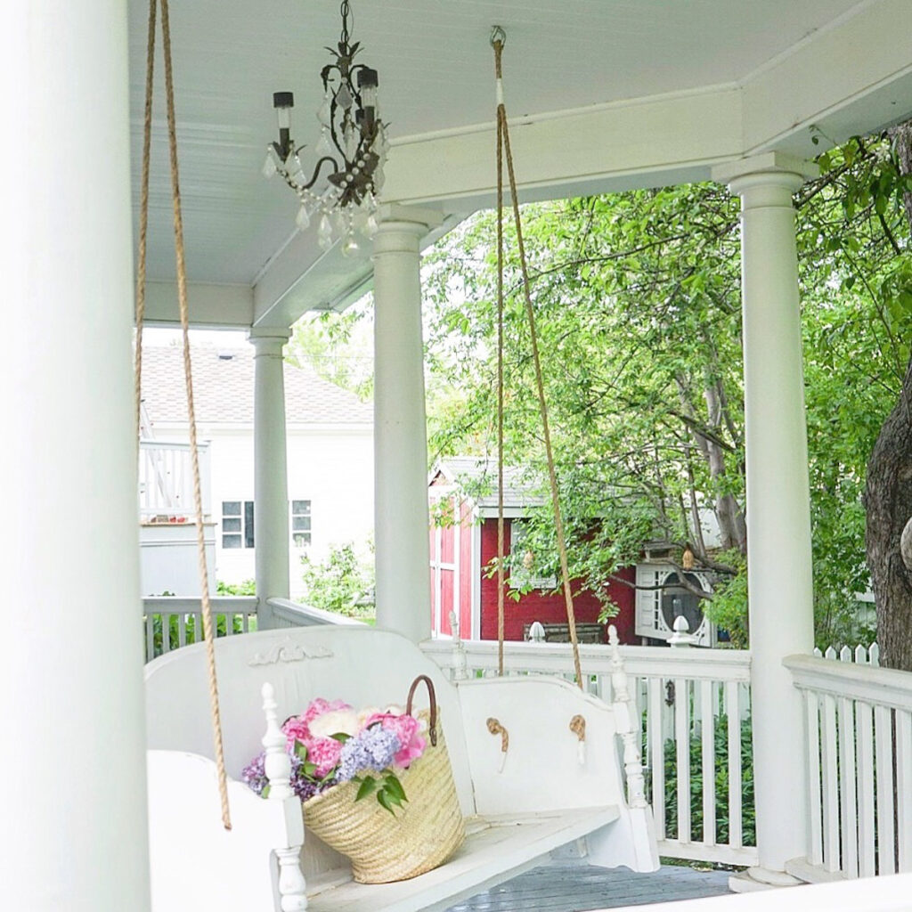 A beautiful porch swing with a market basket in it, wrap-around deck. 