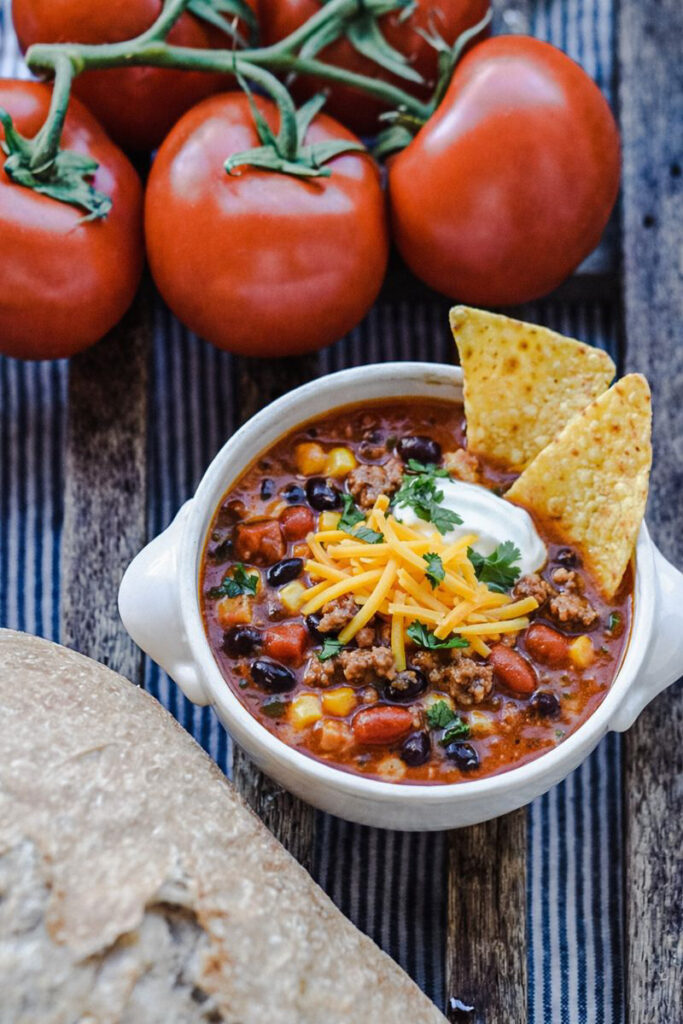 Taco soup in a white bowl, served with shredded cheese and sour cream. 