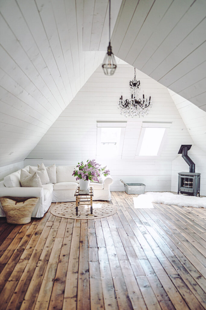 Angled ceilings in an attic space with skylights, a fireplace, floor-to-ceiling windows, chandeliers, and a white sofa. 