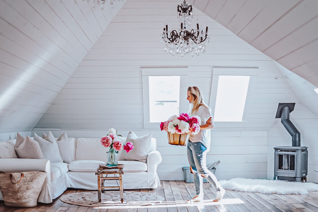 Deborah from B Vintage Style, carrying a basket full of peonies, in her attic space family room.