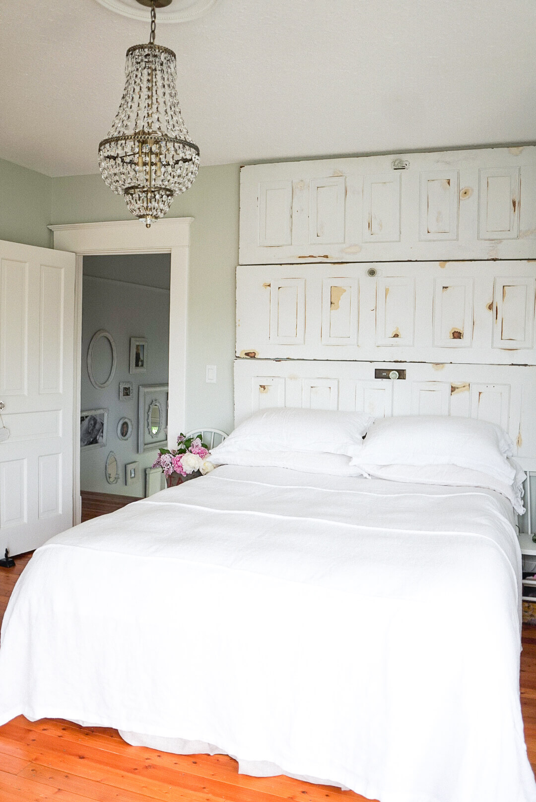 master bedroom salvaged door headboard farmhouse chandelier white linen sheets