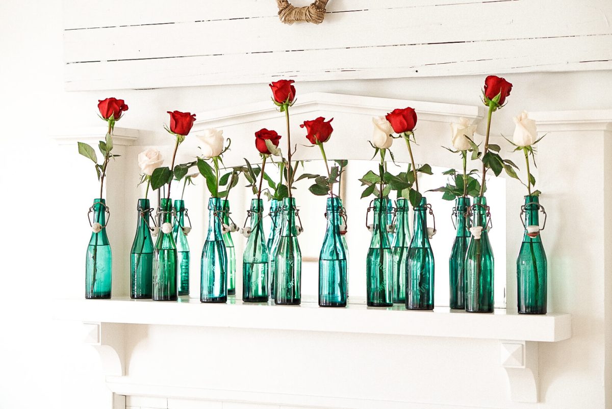fireplace mantle with red and white roses placed in vintage blue bottles. caring for roses in vases