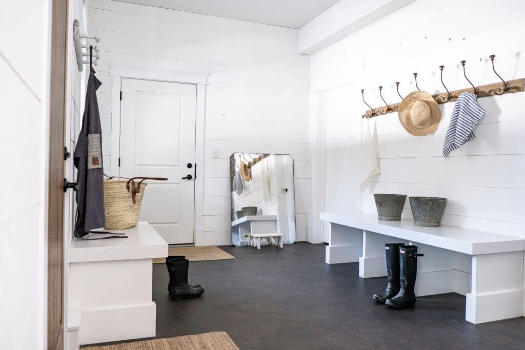 Two stone benches used in a mudroom with hooks and white shiplap walls.