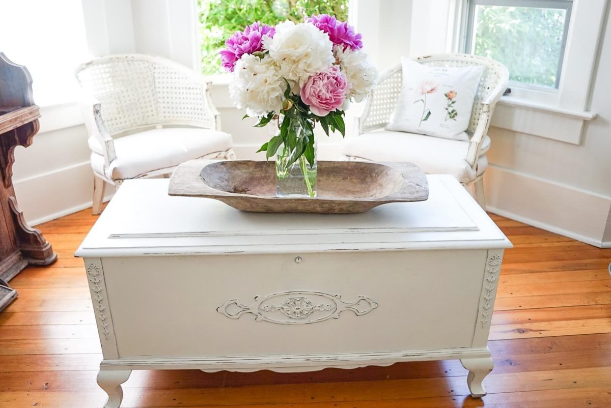 A cedar chest being used as a coffee table with peonies on it.