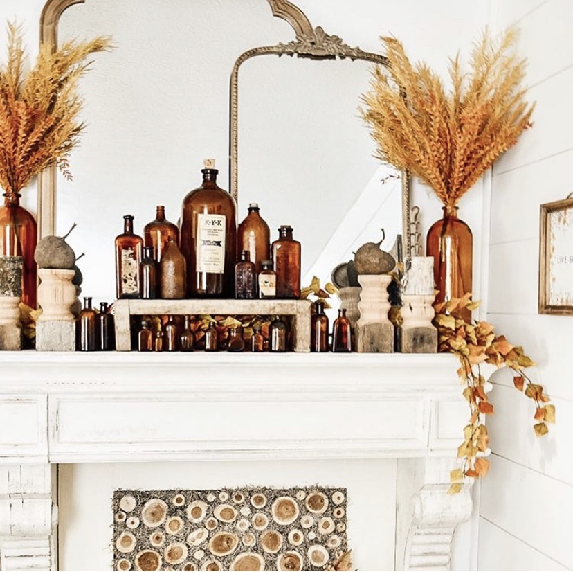 fall home decor amber bottle collection on faux fireplace mantle layered decor mirror pampas grass