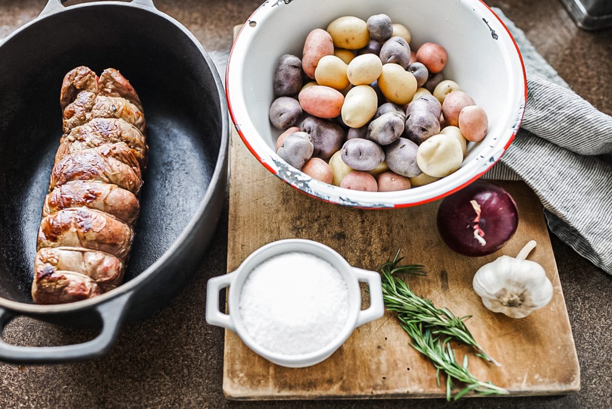beef roast in cast iron dish with a bowl full of colorful potatoes fall apart top round roast ingredients laid out