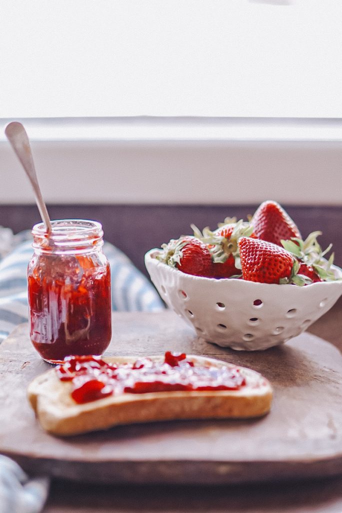 Strawberry jam without pectin in a mason jar beside a bowl of strawberries and a piece of toast with strawberry  jam
