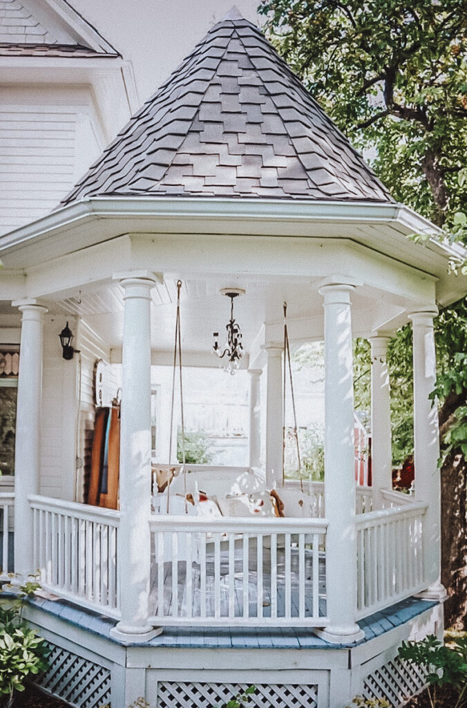 A beautiful gazebo attached to a 1903 Queen and Victorian home with a porch swing in it and a chandelier. 