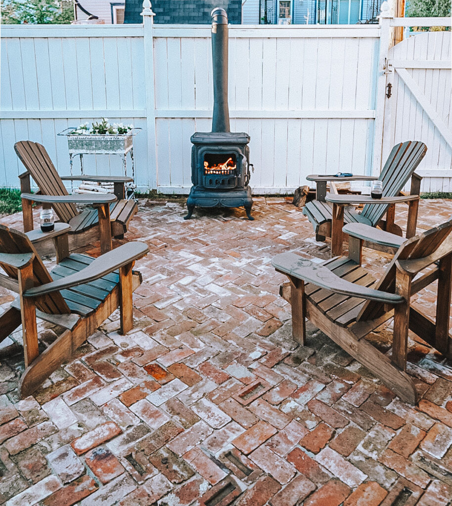 An outdoor wood-burning fireplace with Adirondack chairs around it.