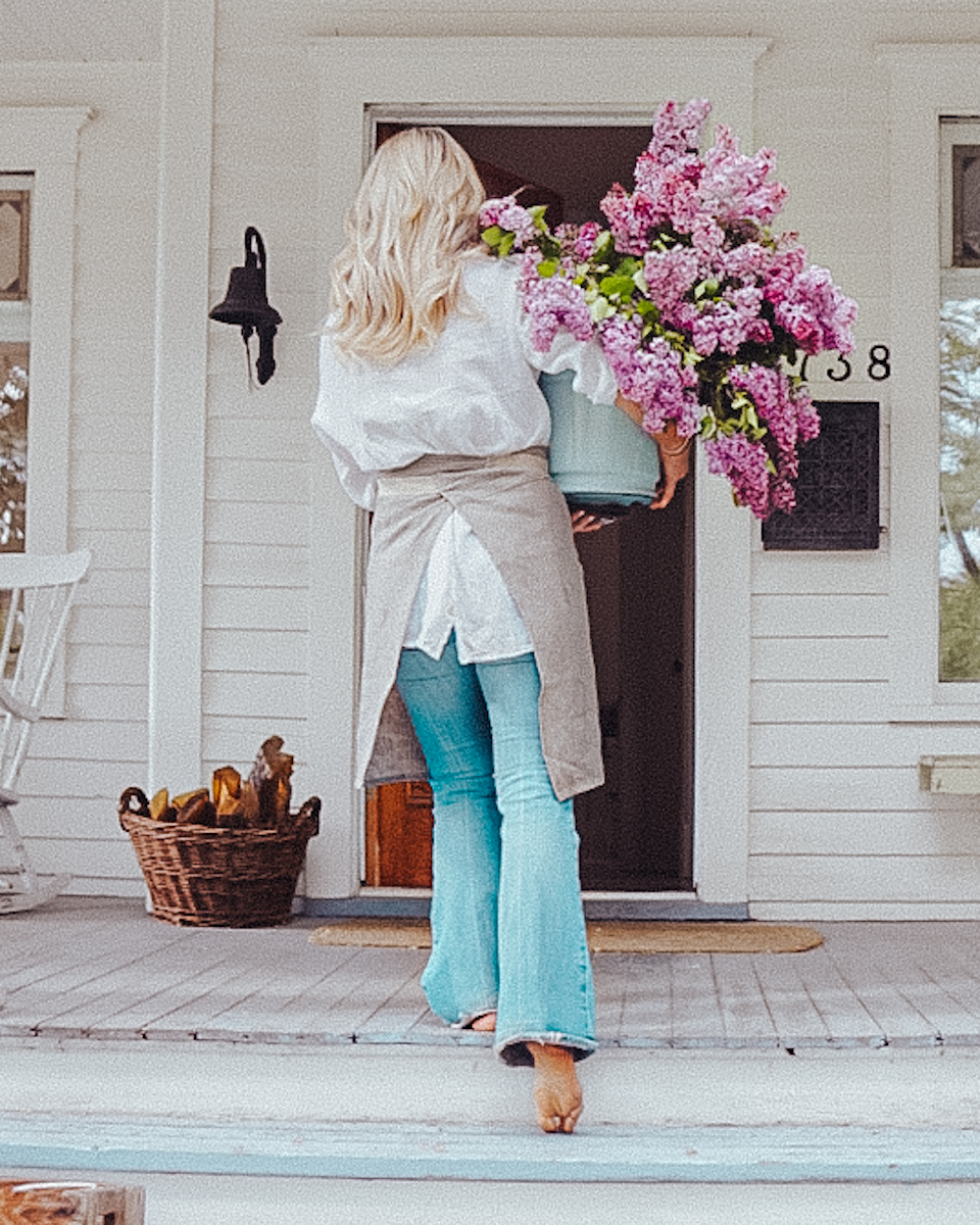 linen apron-02 girl wearing a waitress apron and carrying a bucket of lilacs into a home