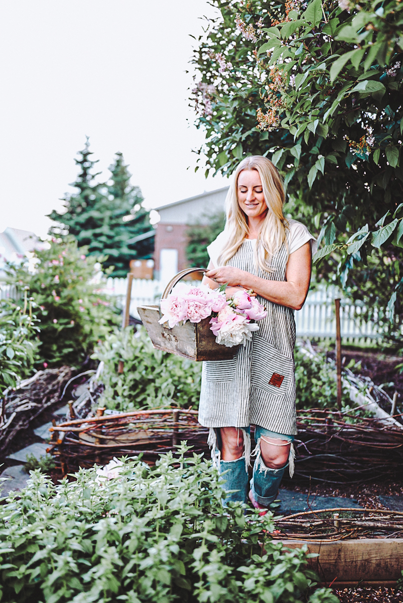 linen apron-13 girl standing in a garden with a bucket of peonies wearing a pinafore apron