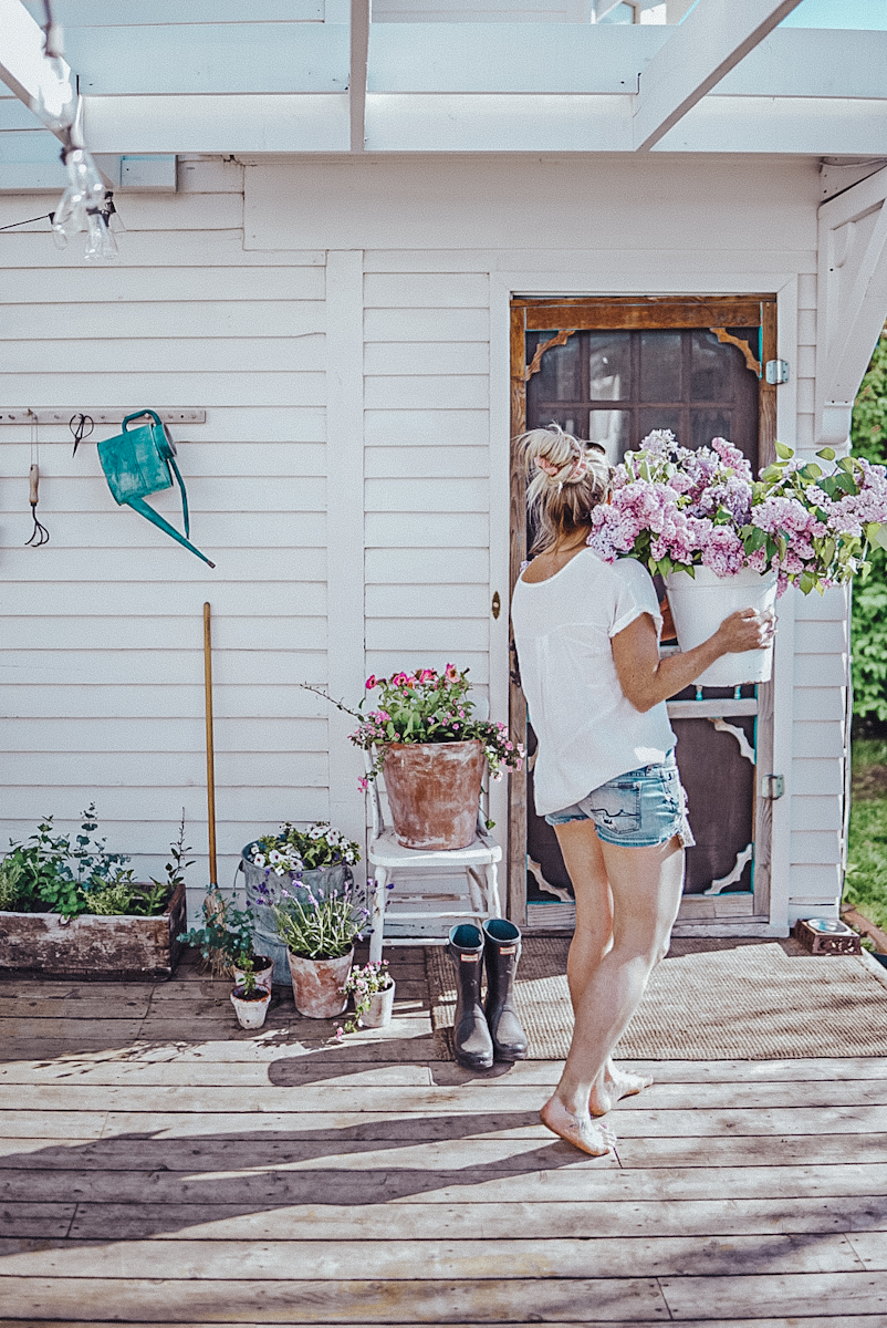 girl carrying lilacs on a patio with flower pots displayed