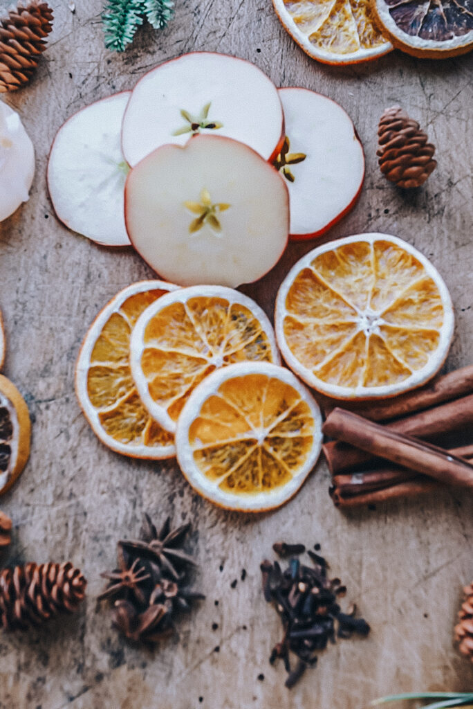 Dried apple and orange slices sit on a cutting board along with pinecones and cinnamon sticks.