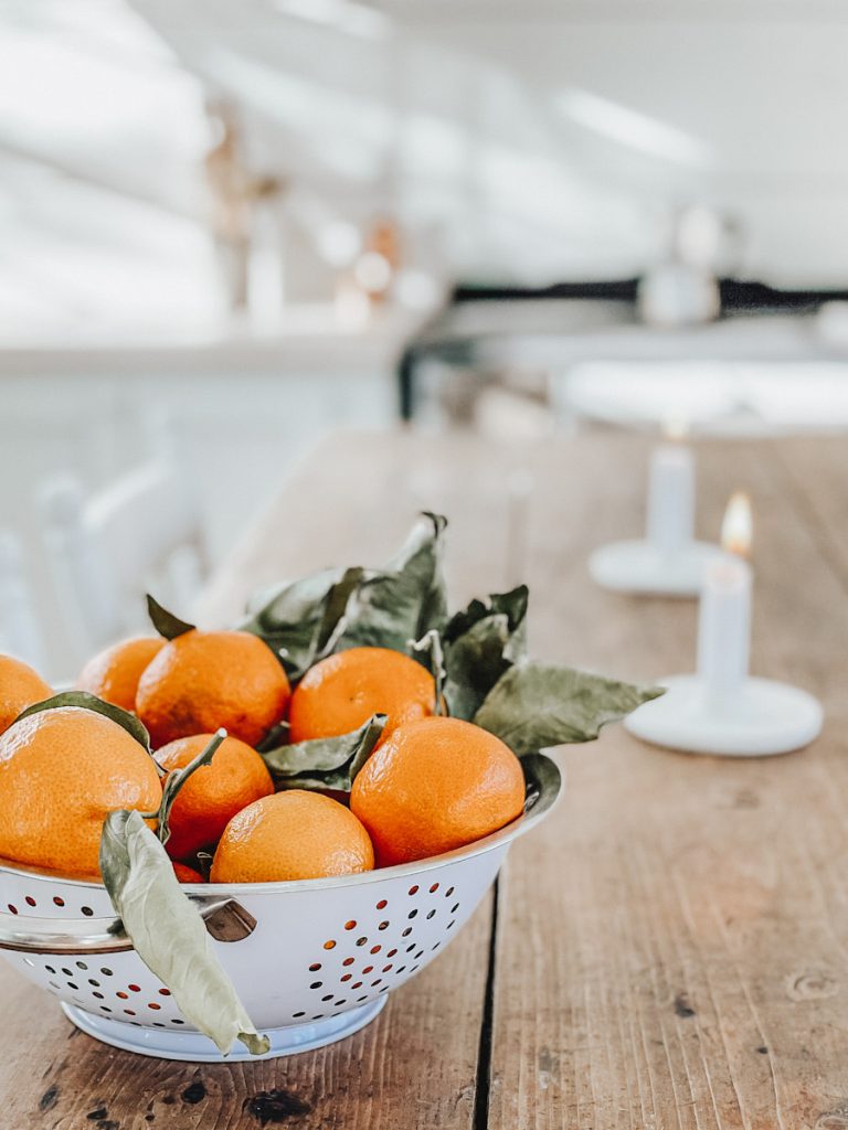 non Christams winter decorations of oranges in a colander and candles on a table