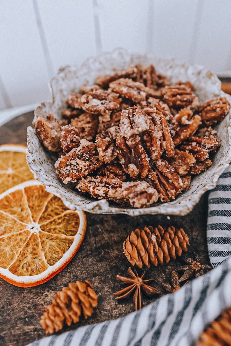 caramelized pecans in a bowl with dried orange slices and pinecones around it.