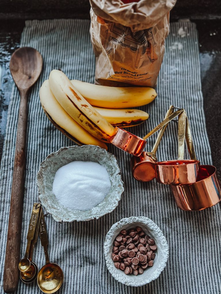 ingredients to make no butter banana bread including bananas, sugar, chocolate chips and flour