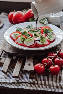 pouring balsamic reduction onto tomato mozzarella basil salad