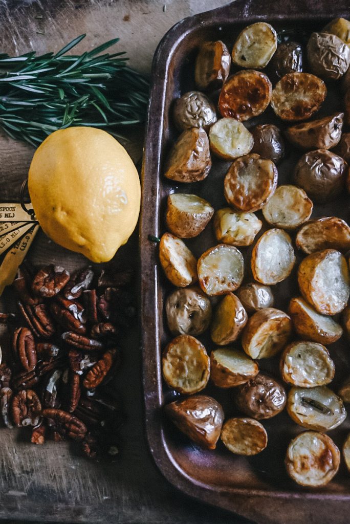 Roasted baby potatoes on a baking tray to make pesto potato salad with toasted pecans and a lemon.