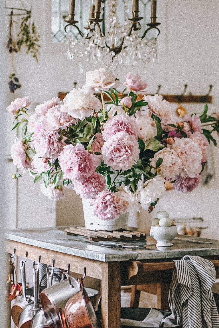 a huge beautiful bouquet of peonies arranged in a white bucket on a kitchen island under a chandelier