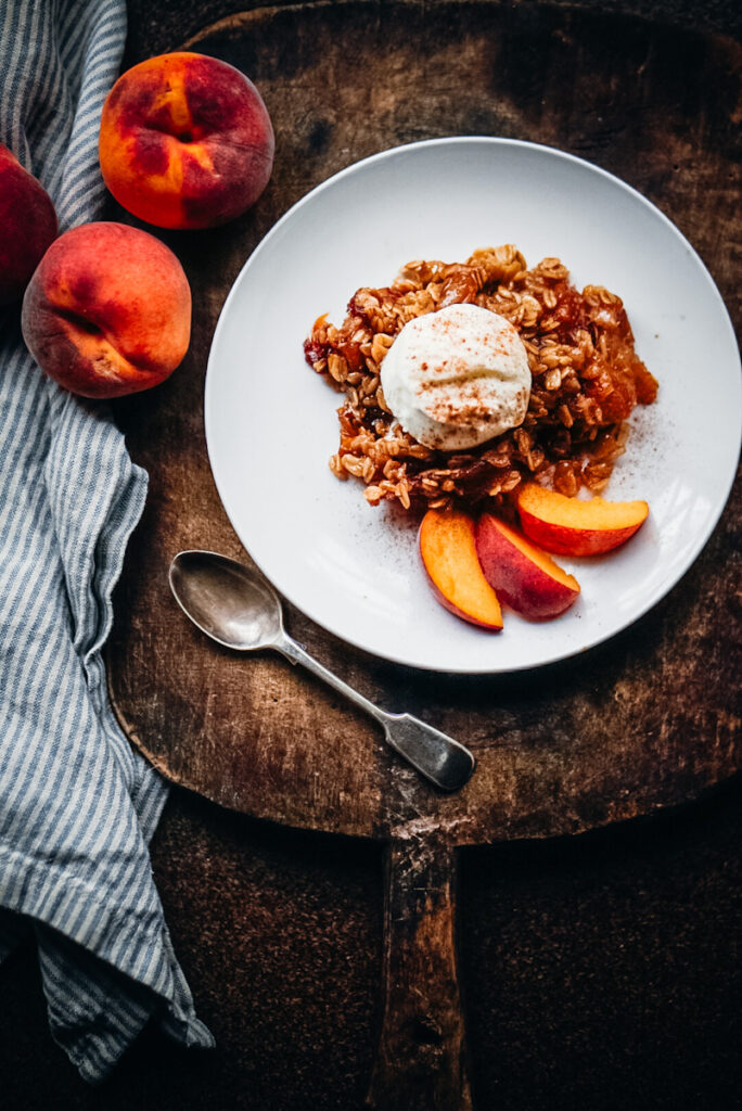 Easy peach crisp on a plate with vanilla ice cream and cinnamon sprinkled on top.