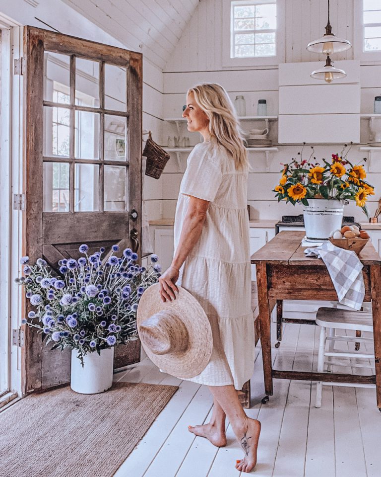 Deborah standing in front of the front door at the tiny home with flowers on the table.