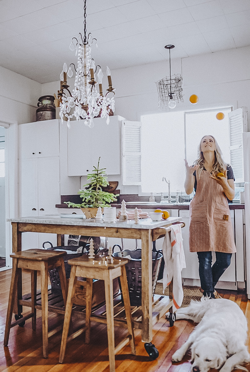 Deborah juggling oranges in the kitchen with a white dog on the floor.