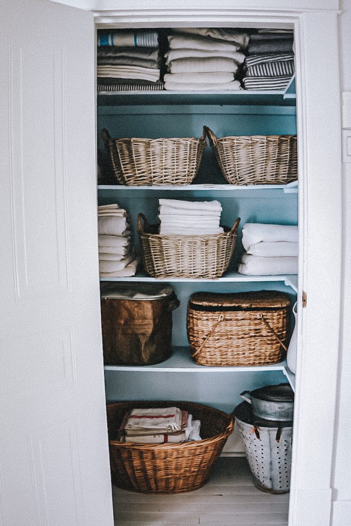 Full view of a linen closet that is beautifully organized with linens folded neatly, baskets and storage containers.