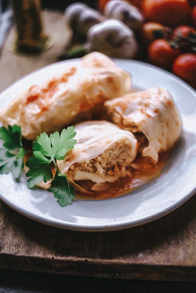 Cabbage rolls displayed on a white plate that have been cut in half and the meat and rice filling showing in the middle.
