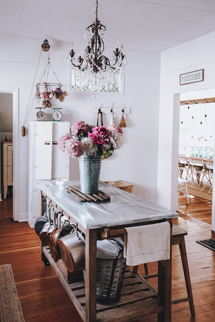 Victorian Farmhouse kitchen with a cart island with pots and pans hooked on the side and flowers on top of the island.