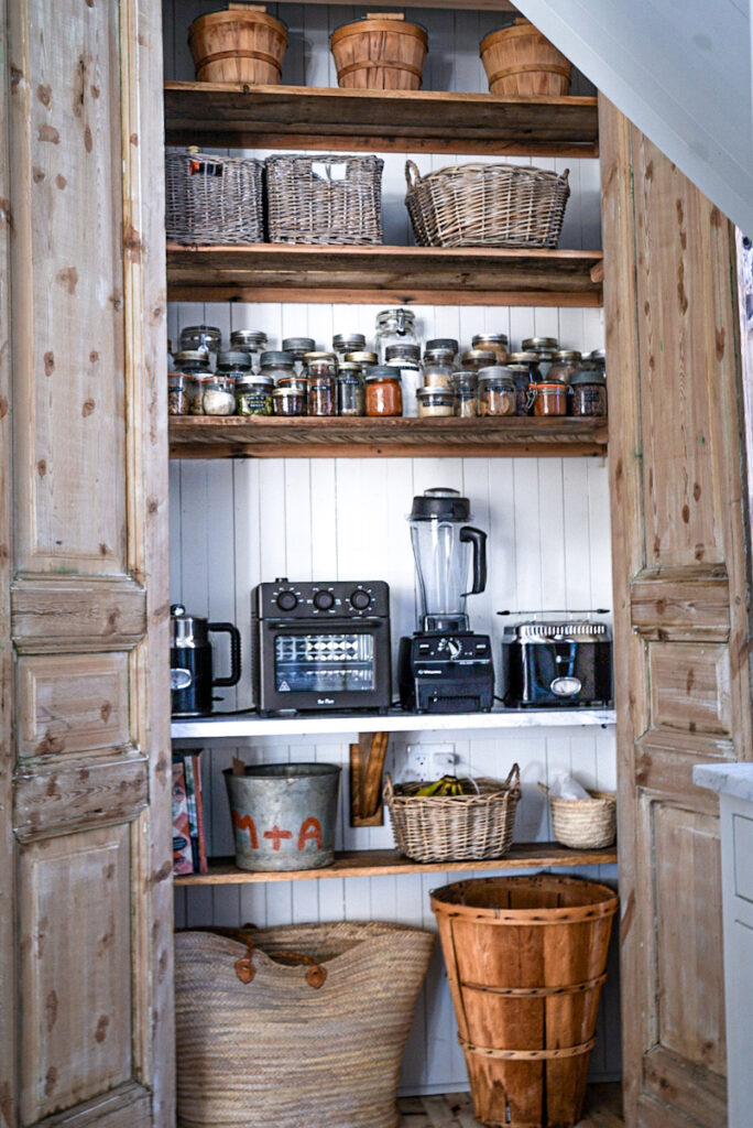 An pantry that has storage for small appliances and baskets and jars that keep everything organized.