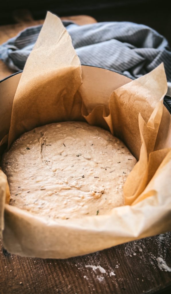 Parmesan rosemary bread in a parchmentw lined Dutch oven ready to be baked.