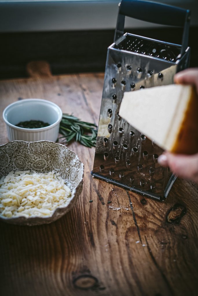 Grating parmesan cheese to make rosemary parmesan bread on a cheese grater.