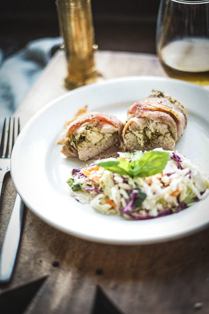 A plate of bacon wrapped stuffed chicken with pesto and goat cheese and a side of mint coleslaw.