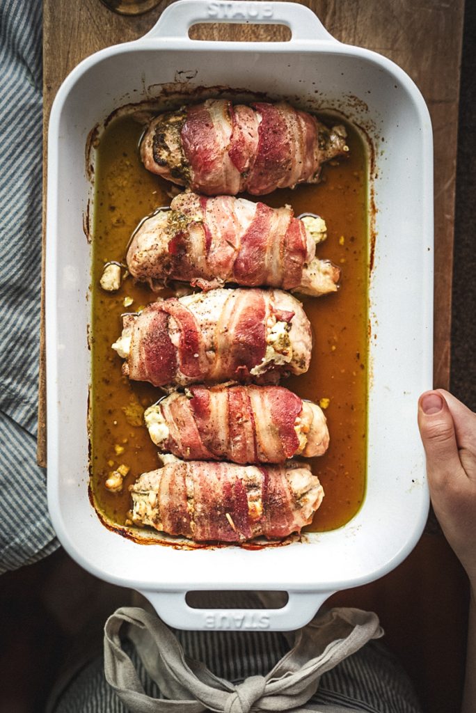 Dish of baked pesto and goat cheese stuffed chicken breast that has been wrapped in bacon and just baked.