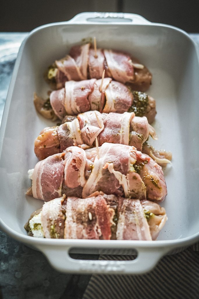 Cooking dish full of stuffed chicken breast with goat cheese and pesto ready to go in to the oven.