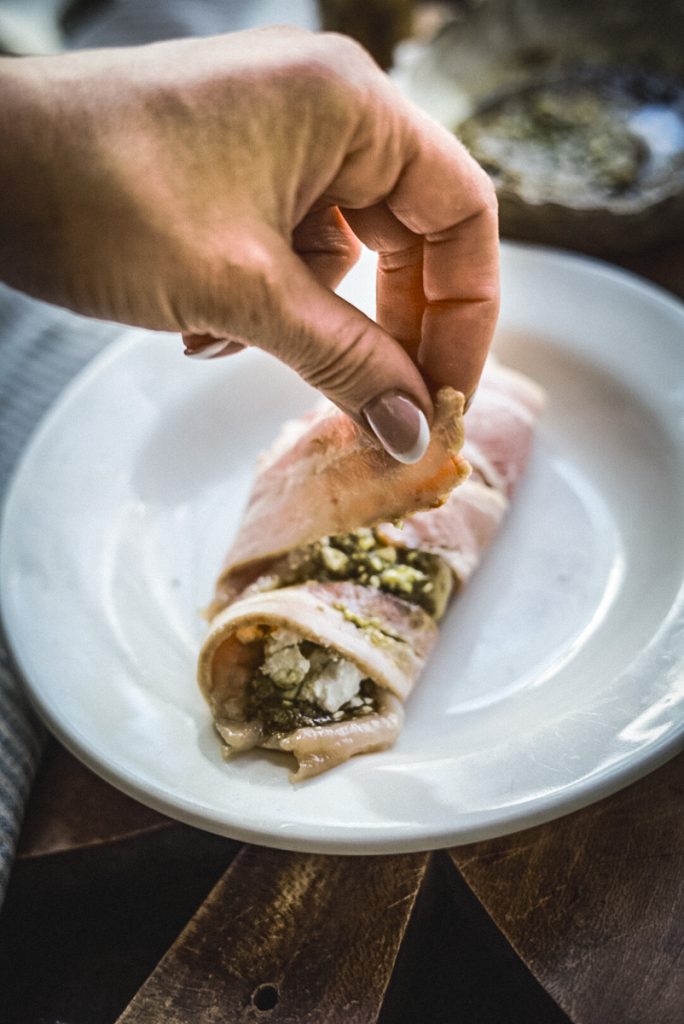 Wrapping stuffed chicken with bacon before baking it.