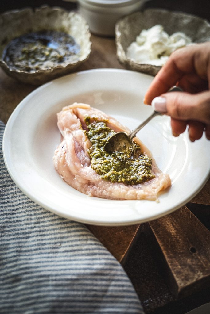 Adding pesto to the centre of a cut chicken breast.