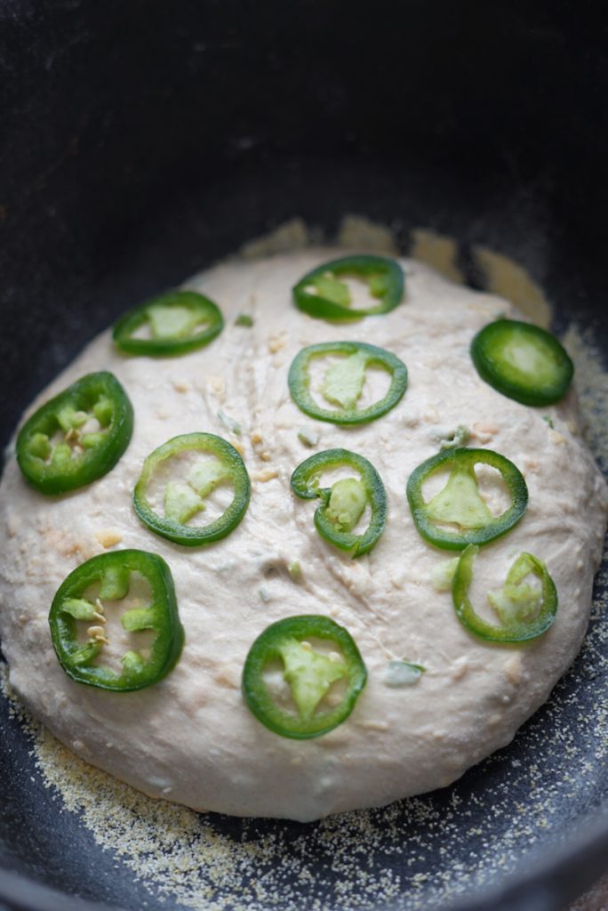 Adding jalapenos on top of the dough before baking the bread.
