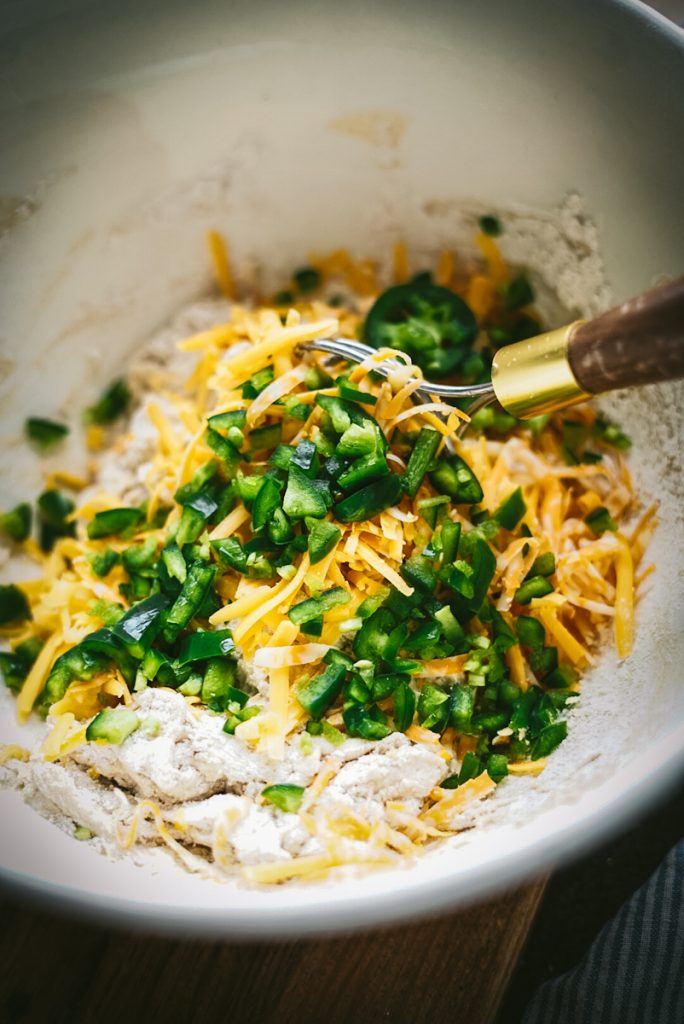 Adding cheddar cheese and jalapeno peppers to the bread dough to make bread.
