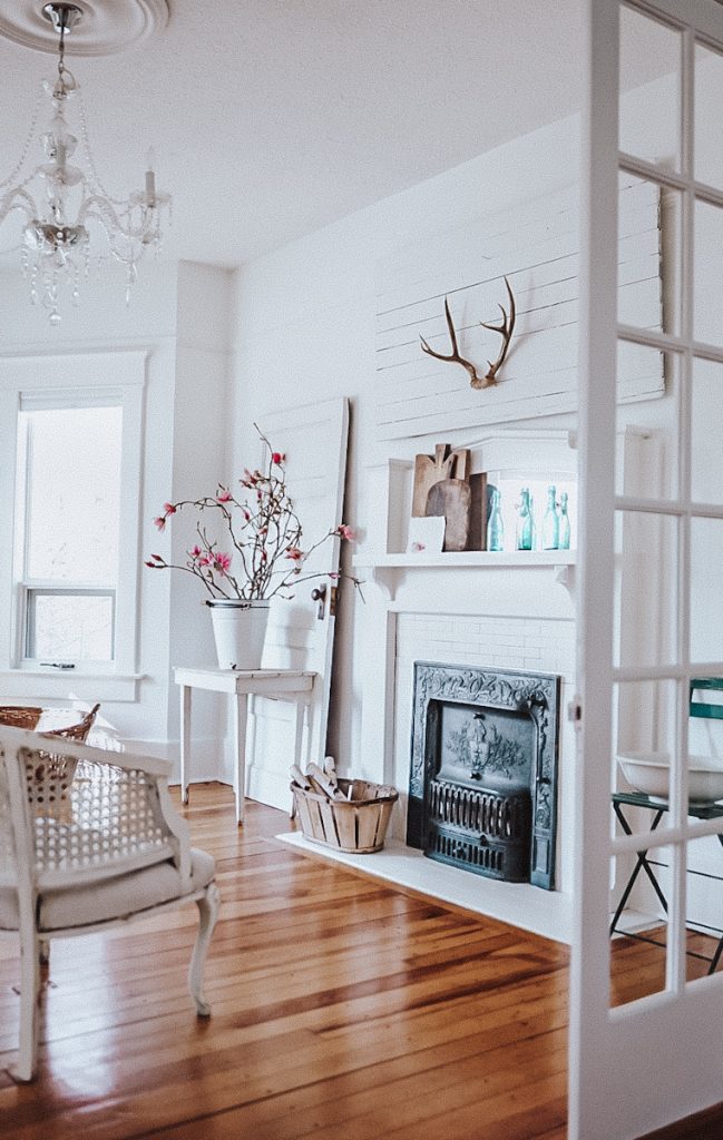 Beautiful fireplace in a historic house that has antlers above it and a bucket of magnolia flowers beside it.