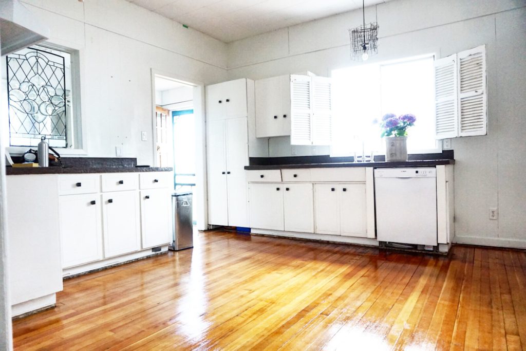 A white kitchen with shutters on the window and beautiful original wood floors.