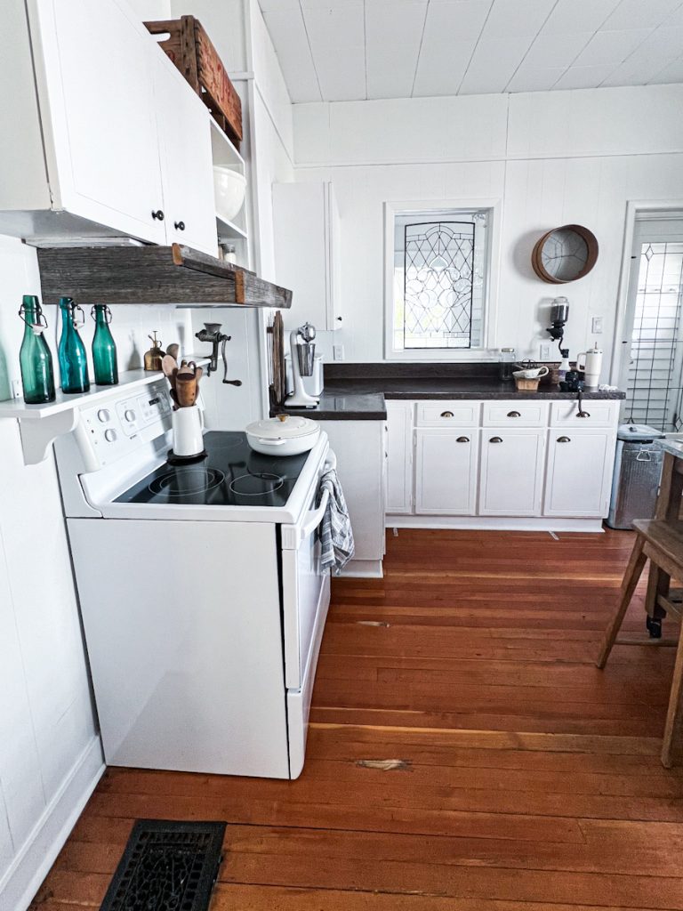 The view of a white kitchen with an antique lead window transom.