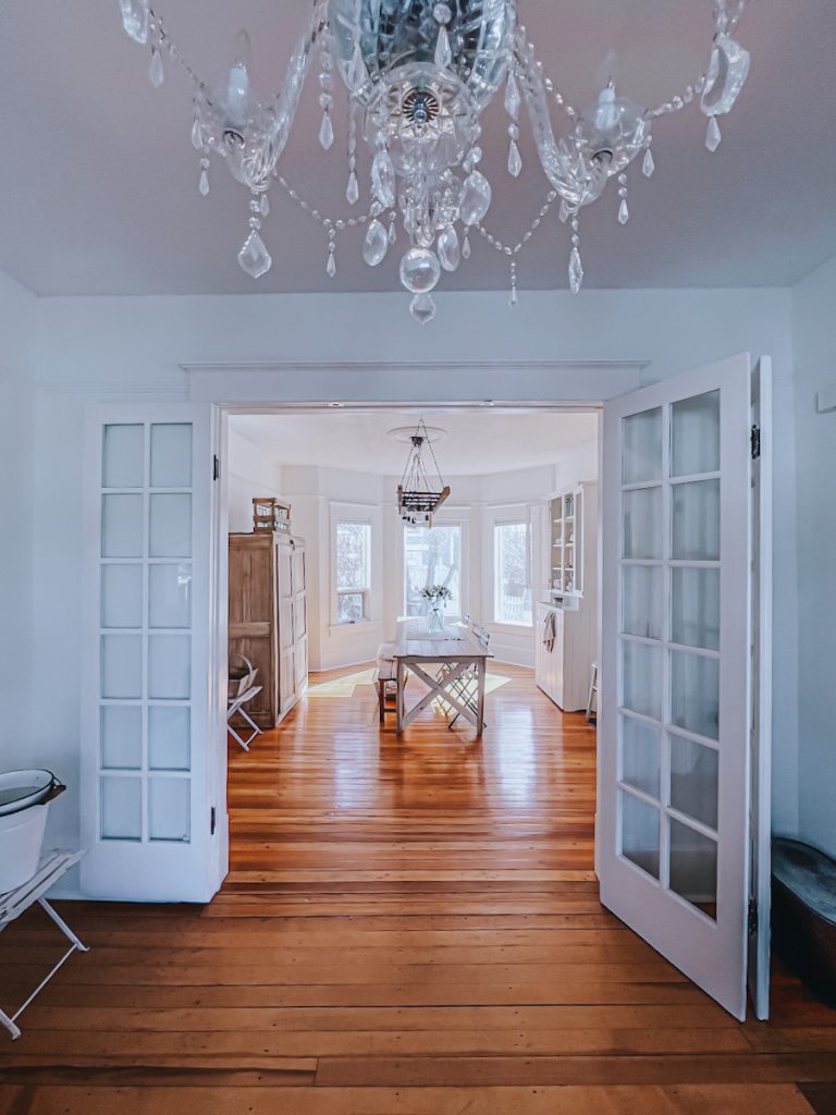Triple french doors that are at the entrance of a beautiful white dining room space with a farmhouse table.
