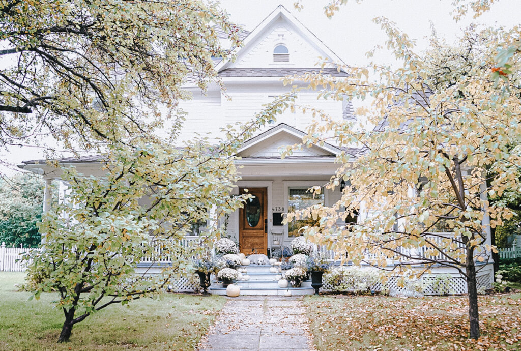 A beautiful white 120 year old house that has trees in front of it.