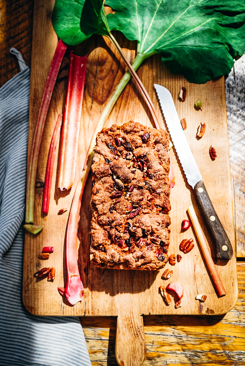 Rhubarb bread on a wood cutting board next to rhubarb pieces.