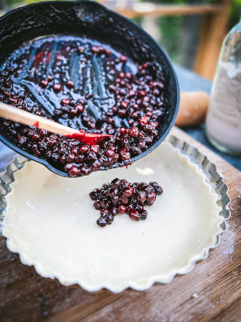 Adding Saskatoon pie filling to a pie shell.