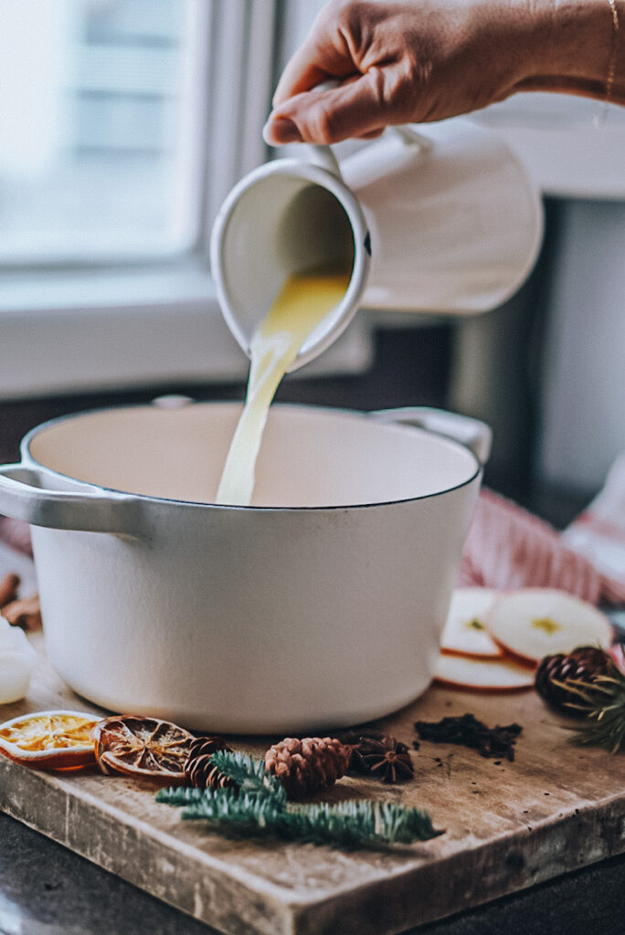 Adding orange juice into a pot to make mulled cider.