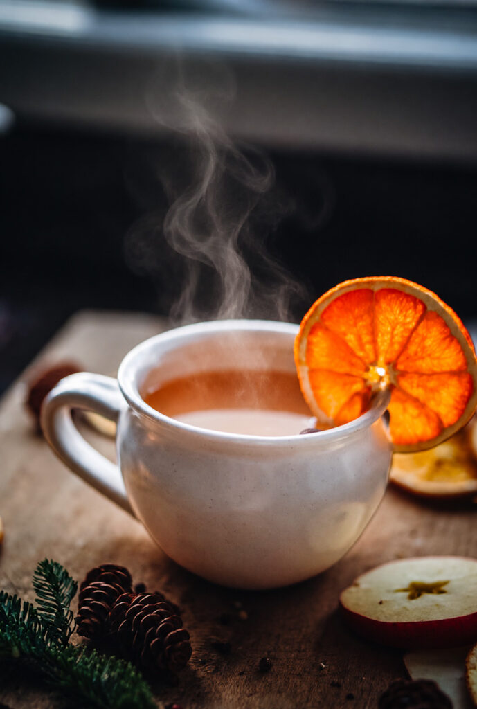 A delicious cup of steaming hot homemade apple cider garnished with an orange slice.