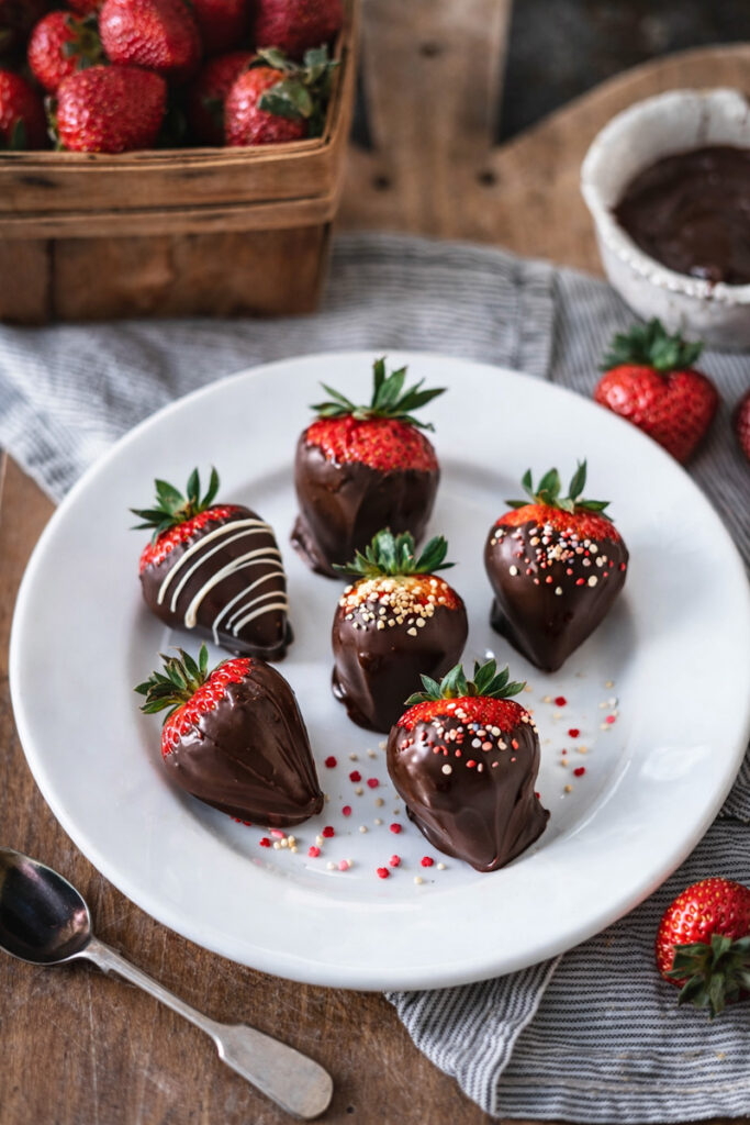 Dark chocolate-dipped strawberries covered in sprinkles and nuts on a white plate 