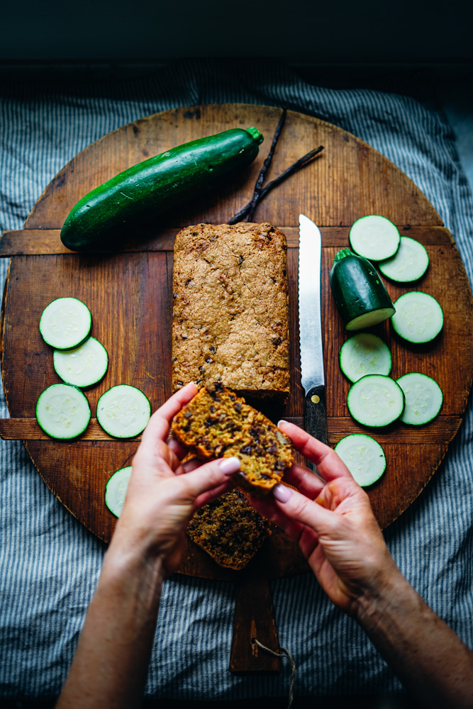 Zucchini full of chocolate chips that has been slices on a cutting board with fresh zucchini.